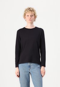 Zwarte lange mouwen shirt van zachte stof, met een ronde hals en een relaxed fit, gecombineerd met lichtblauwe denim jeans.