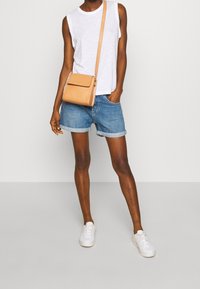 Bílé tílko bez rukávů, modré džínové šortky s ohrnutými lemy, béžová kabelka přes rameno a bílé tenisky. Jednoduchý, ležérní outfit.