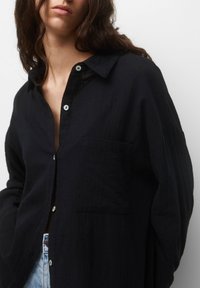 Camicia nera con bottoni, realizzata in tessuto testurizzato, dotata di una tasca sul lato sinistro e leggeri bottoni, con una vestibilità rilassata.
