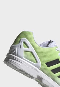 Green textured athletic shoe with white sole, featuring black stripes and a unique heel design. Laces and padded collar in contrasting white.