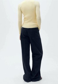 Schwarze Jeans mit weitem Bein, hoher Taille und Gesäßtaschen. Kombiniert mit einem enganliegenden, gerippten gelben Pullover. Glatte Denim-Textur.