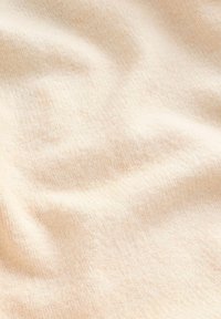 Zacht, lichtgewicht stof in een bleek perzikkleur met een fijne textuur en subtiel, ongelijkmatig weefpatroon, dat zachte golvingen over het oppervlak creëert.