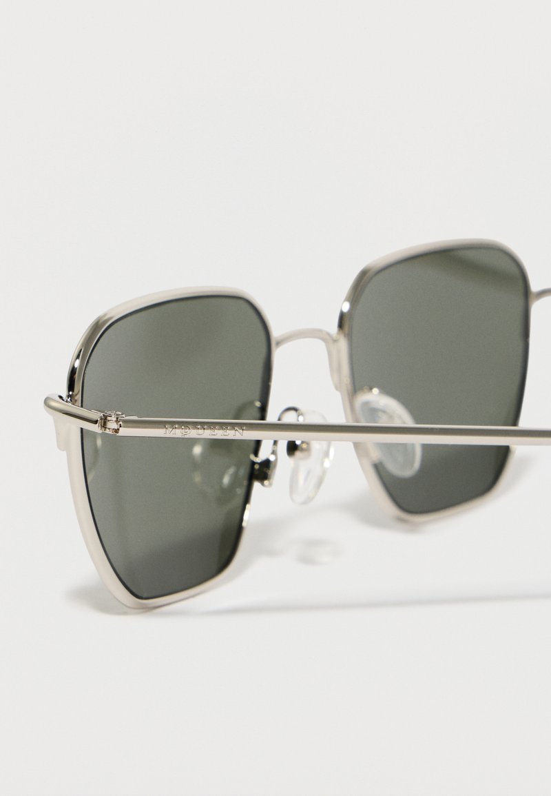 Lunettes de soleil carrées avec montures en métal argenté et verres teintés foncés, dotées de plaquettes de nez ajustables et du mot « McQueen » gravé sur la branche.