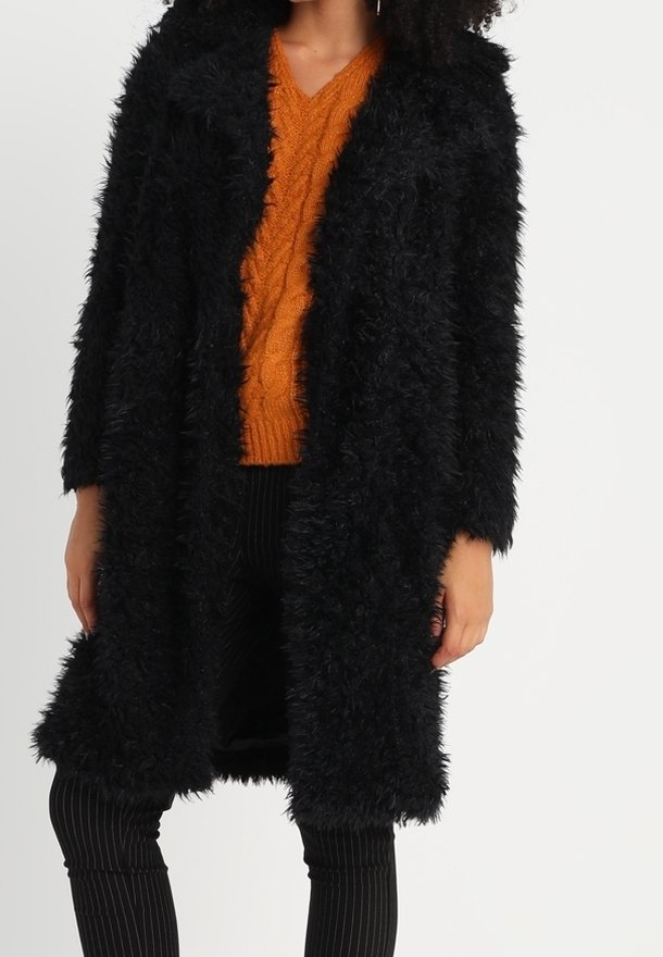 Sort pelsjakke i imiteret pels med lange ærmer og åben front, der har en tekstureret, shaggy overflade og en afslappet pasform.