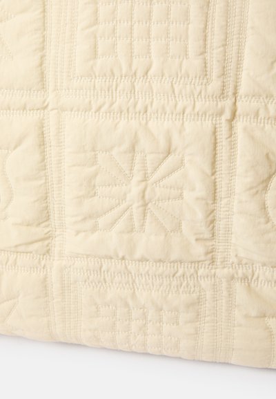 Coperta trapuntata color crema con vari motivi geometrici in rilievo e bordi cuciti, realizzata in tessuto morbido con una superficie leggermente strutturata.