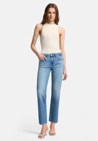 Ljusbeige ärmlös topp i kombination med ljusblå högmidjade jeans med rå fåll. Jeanssen har en avslappnad passform och diskret blekning.