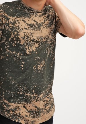 Green and tan short-sleeve t-shirt featuring a splatter pattern, round neckline, and soft fabric texture. Regular fit.
