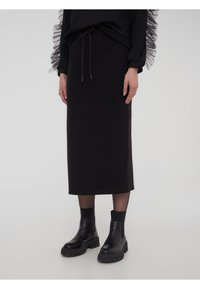 Gonna midi nera in tessuto morbido, con vita con coulisse e abbinata a stivaletti neri chunky per creare contrasto.