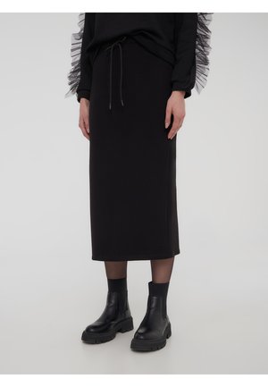 Gonna midi nera in tessuto morbido, con vita con coulisse e abbinata a stivaletti neri chunky per creare contrasto.