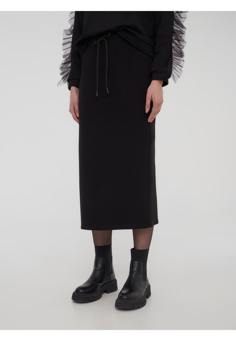 Gonna midi nera in tessuto morbido, con vita con coulisse e abbinata a stivaletti neri chunky per creare contrasto.