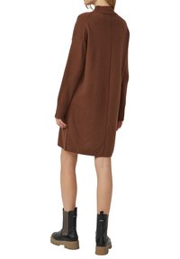 Braunes Strickkleid mit hohem Kragen, gerippten Bündchen und geradem Schnitt; kombiniert mit schwarzen Stiefeletten mit strukturierten Einsätzen.