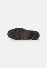 Suela de un zapato con un diseño rugged, hecha de caucho negro. Cuenta con profundos surcos para tracción y tres logotipos circulares en la parte inferior.
