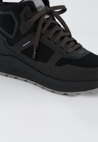 Zwarte waterdichte sneaker met een textuur mesh bovenwerk, bruine veters en een solide zwarte tussenzool. Beschikt over een robuuste loopvlak op de buitenzool.