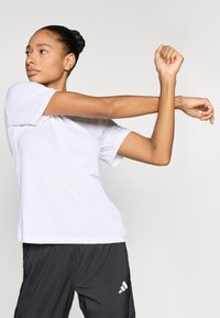 Bijela sportska majica kratkih rukava, laganog materijala, opuštenog kroja. Nošena s crnim sportskim hlačicama s bijelim logotipom.