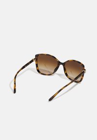 Skallusolbriller i skjoldmønstret med brune gradient linser, kantete design, slanke armer og dekorative gulldetaljer på hengslene.