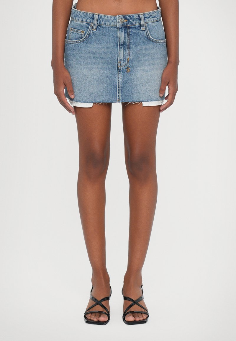 Fustă mini din denim cu un ton albastru deschis, cu margini desfăcute, design cu cinci buzunare și închidere cu buton. Asortată cu sandale negre cu curele.