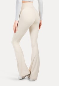Beżowe legginsy rozszerzające się na dole, wykonane z gładkiego, elastycznego materiału, z wysokim stanem i dopasowanym krojem na udach.