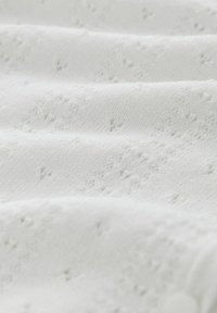 Valge kangas tekstuurse mustriga, millel on väikesed augud. Materjal tundub pehme ja sile, kergete voldide ja langevusega.