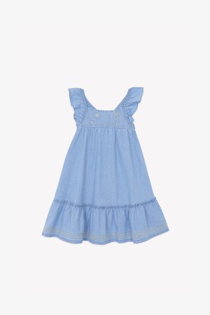 Vestido de chambray azul claro con bordado de un sol y una palmera, tirantes con volantes y una falda con capas que tiene detalles de encaje en el dobladillo.