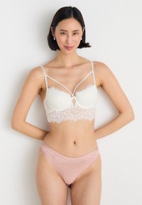 Bralette bianco in pizzo con coppe strutturate e spalline sottili; abbinato a mutandine in pizzo trasparente rosa, entrambe con motivi floreali.