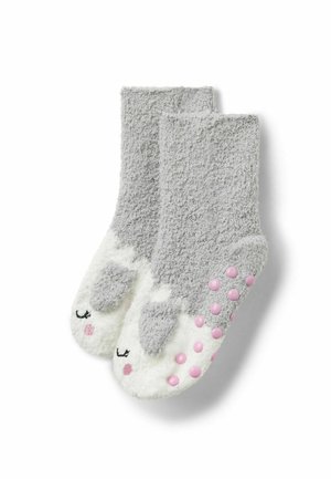 Chaussettes douces grises et blanches duveteuses avec un motif yeux fermés et joues roses, et des grips antidérapants roses sur les semelles.