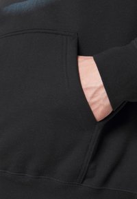 Sudadera negra con bolsillo tipo canguro. Tela suave con un corte relajado. Puños y dobladillo ligeramente acanalados que aportan estructura.