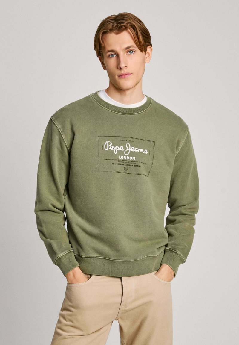 Sudadera verde con cuello redondo y puños acanalados. Presenta un parche de logotipo en la parte frontal que dice "Pepe Jeans London". Está hecha de un tejido suave.
