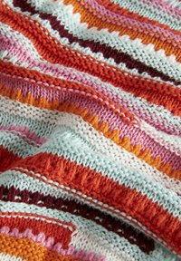 Tela de punto multicolor con rayas onduladas en rojo, rosa, naranja y azul claro, que presenta patrones texturizados y varios tipos de puntadas.