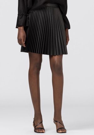 Black pleated skirt made from a smooth material, featuring a fitted waist and a flared hem. Worn with black strappy sandals.