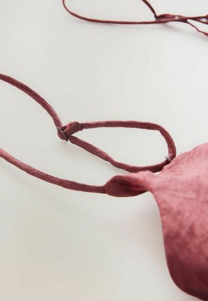 Reggiseno in tessuto mauve con spalline sottili, caratterizzato da una forma circolare e una superficie liscia. Include un piccolo dettaglio hardware regolabile.