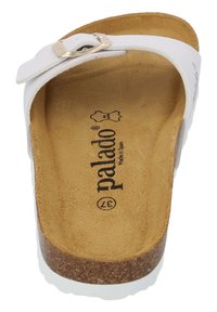 Vit sandalslide med en glänsande metallspänne, brunt mockainlägg och en korkliknande sula med texturerade vita kanter. Varumärkeslogotyp på inlägget.