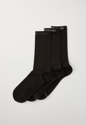 Chaussettes en coton noires de type crew, avec un poignet côtelé et un logo discret sur le dessus. Trois paires présentées avec une texture lisse.