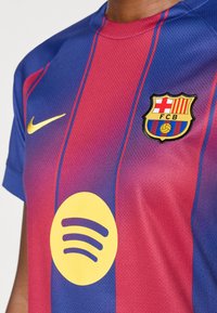 Barcelona-témájú mez, vízszintes kék és piros csíkokkal, arany Nike logóval, sárga Spotify logóval és FCB címkével.