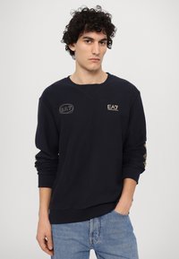 Jūras spēku svīteri ar ribotu kakla un piedurkņu apdari, ar zelta EA7 logo uz krūtīm un piedurkņa. Strukturēta auduma izstrādājums ar brīvu piegriezumu.