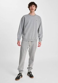 Grå bomulls-sweatshirt och matchande sweatpants med elastisk midjeresår, med en liten logotyp på bröstet och ribbade muddar. Svarta sneakers.