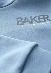Svijetloplavi dukserica od mekog materijala, s teksturiranim uzorkom i logom "BAKER by TED BAKER" u tamnijoj sivoj boji ispisanim.