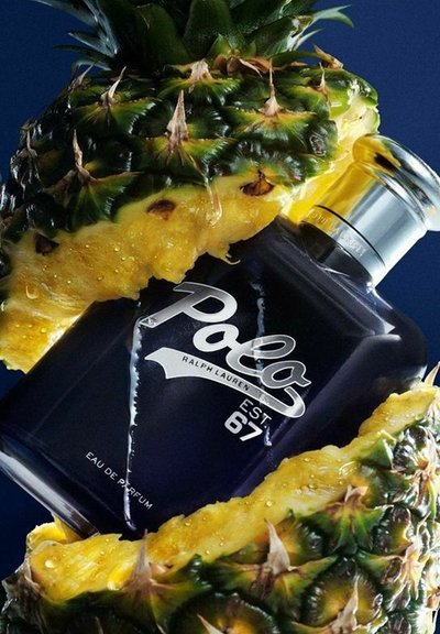 En mörk flaska av Polo Ralph Lauren-parfym är delvis innesluten i en färsk, saftig ananas, vilket framhäver ett fräscht tropiskt tema.