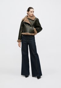 Giacca in pelle nera con fodera e polsini in pelliccia marrone, abbinata a pantaloni denim scuri a gamba larga a vita alta e stivali neri con tacco.