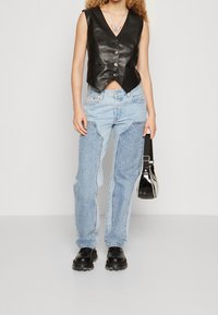 Czarna skórzana kamizelka na krótko z zapięciem na guziki, zestawiona z jasnoniebieskimi zniszczonymi dżinsami. Czarne ciężkie buty i mała czarna torebka.