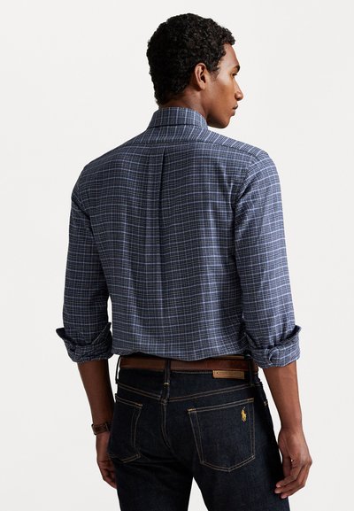 Blå rutete skjorte med høy krage, rullede ermer og bakfeller. Kombinert med mørk denim jeans med lærbelte.