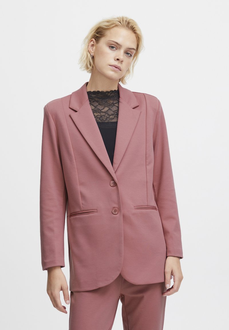 Blazer aus leicht rosa Stoff, mit geschlitztem Revers, zwei Knöpfen und Seitentaschen. Glatte Textur mit tailliertem Schnitt.