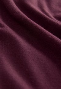 Tissu doux de couleur violet foncé avec une texture fine visible et des plis doux créant des ombres lisses.