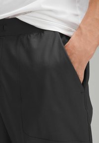 Schwarze Sportshorts mit glatter Textur, elastischem Bund und Seitentaschen. Das Design ist einfach und funktional.