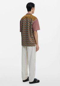Short-sleeve shirt featuring a colorful zigzag pattern, with a multi-colored back and a collared neck; worn with striped pants and black slide shoes.