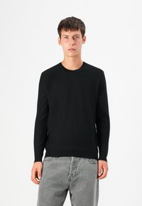 Pulover negru tricotat cu guler rotund, mâneci lungi și o siluetă ajustată. Materialul pare neted și moale, cu detalii minime.