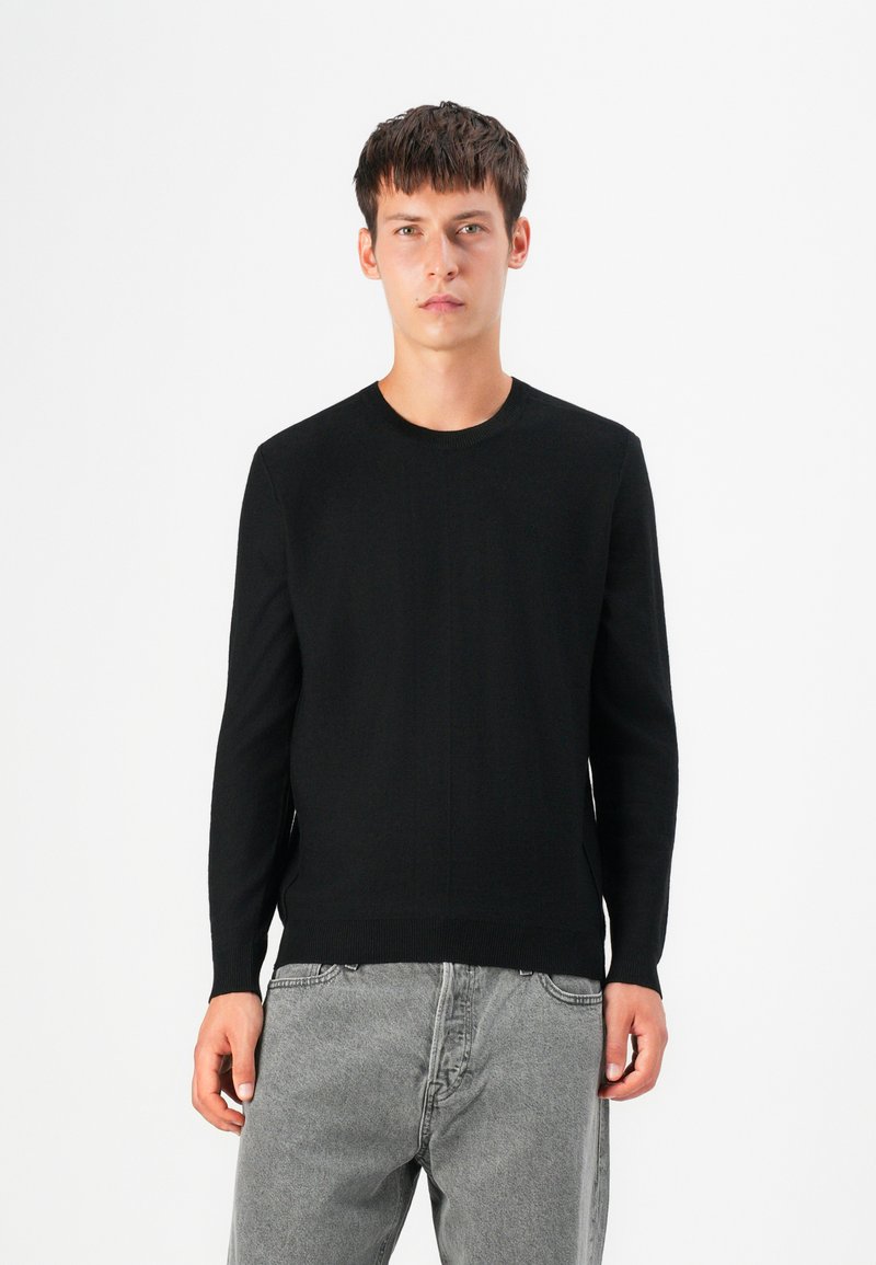 Maglione nero lavorato a maglia con scollo rotondo, maniche lunghe e una silhouette aderente. Il tessuto appare liscio e morbido con dettagli minimi.