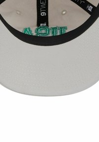 Gorra de béisbol gris claro con visera negra. Presenta bordado verde en la parte inferior. El interior incluye etiquetas con la talla y la marca.