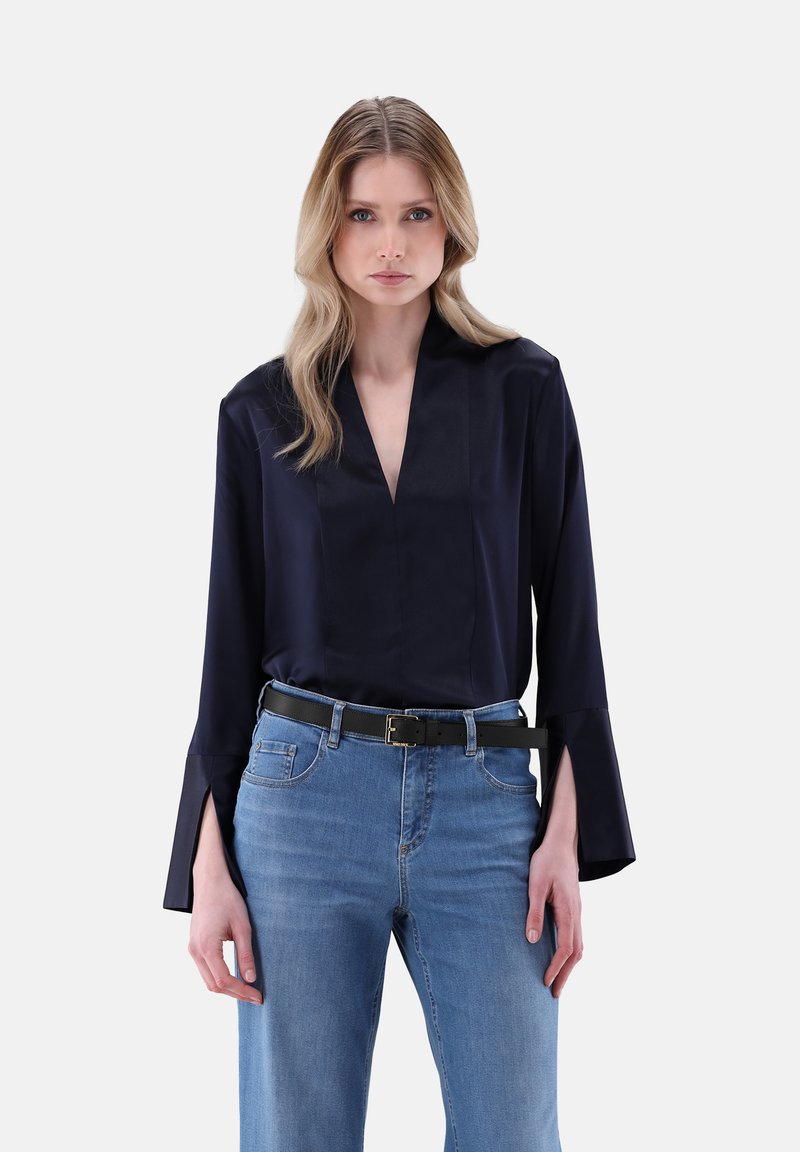 Blusa di raso blu navy con scollatura a V e maniche a campana, abbinata a jeans in denim azzurro chiaro e a una cintura nera con fibbia quadrata.
