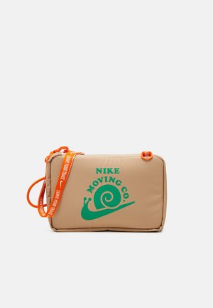 Bolso de hombro rectangular beige de Nike con logo de caracol verde y texto "NIKE MOVING CO.", con correa naranja que tiene el texto "LEAVE YOUR TRACE".