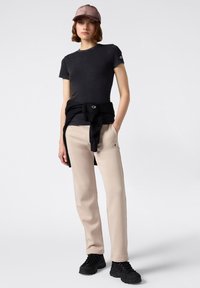 T-shirt nera a maniche corte, pantaloni felpati beige con logo, felpa nera legata in vita e calzature nere. Materiali morbidi e casual.